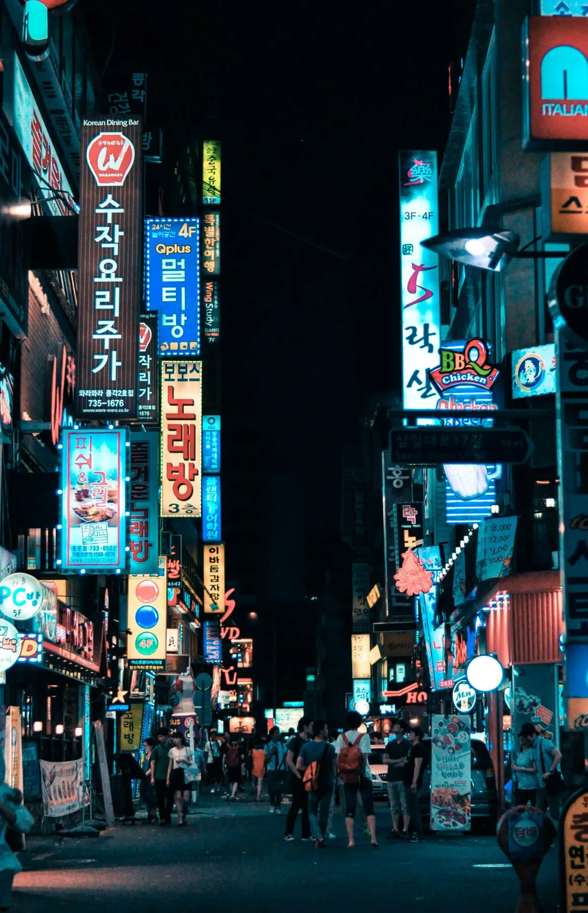 A neon-lit street at night, signs stacked above a crowd