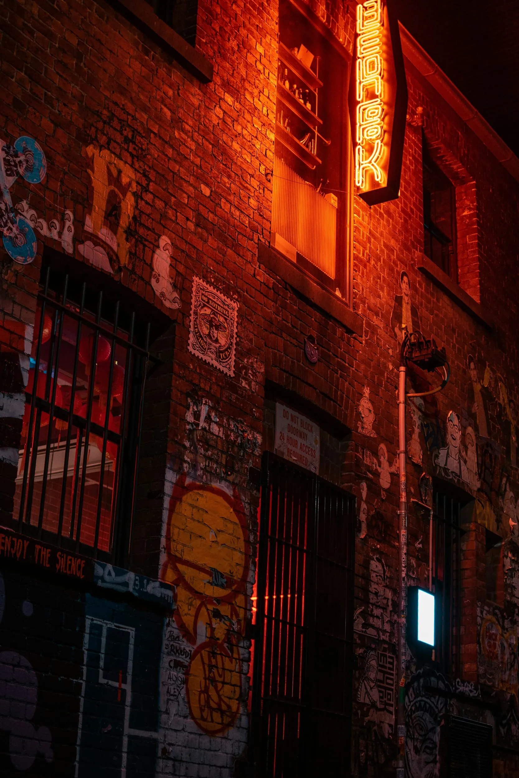 An orange neon blade sign on a brick laneway wall