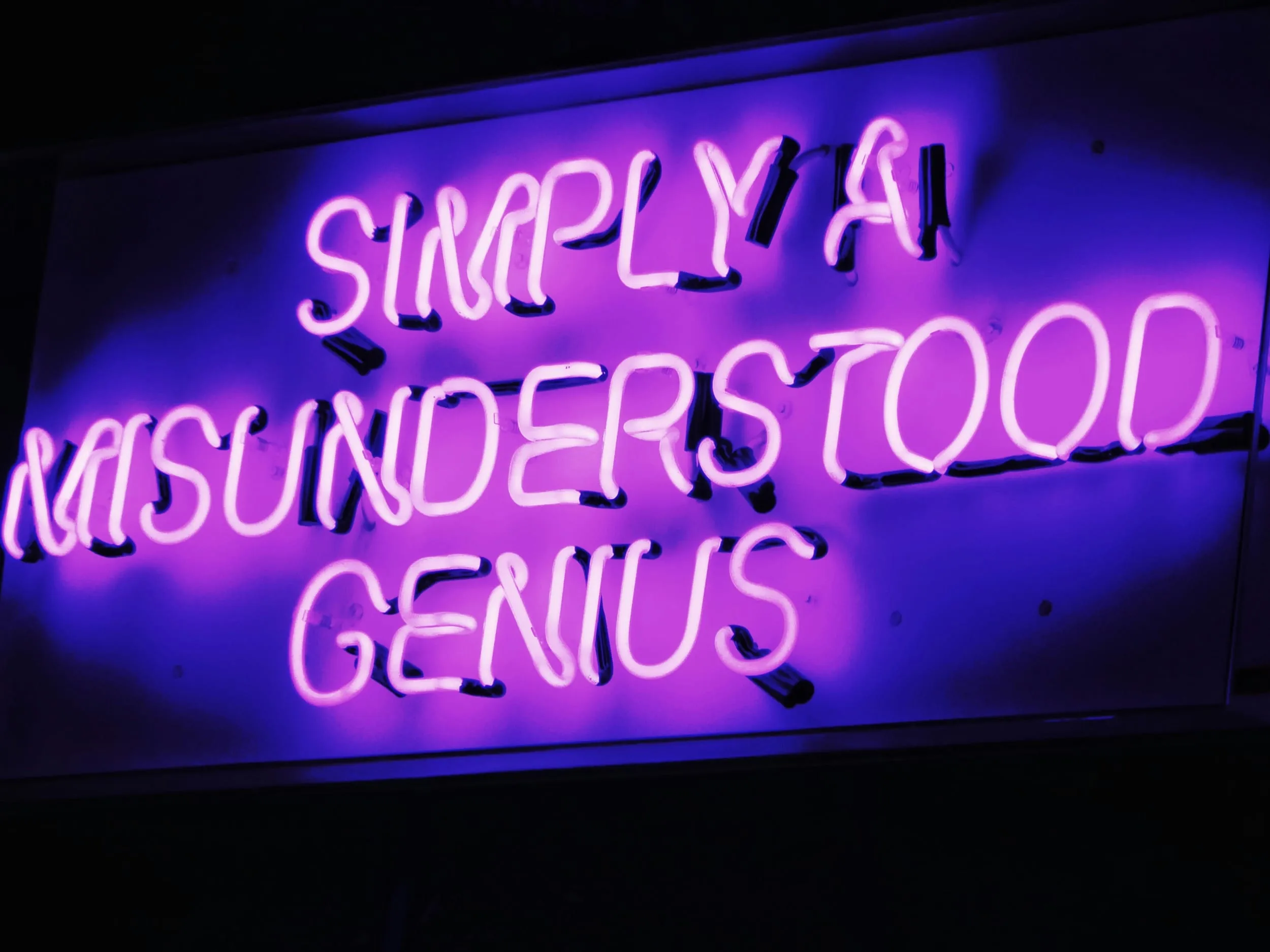 A purple neon sign reading Simply a misunderstood genius