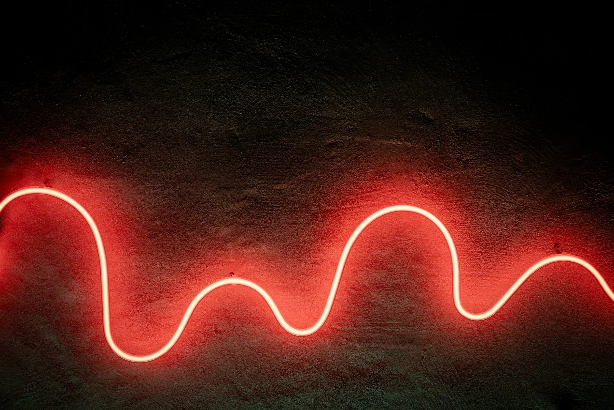 A single red neon tube curving across a dark concrete wall