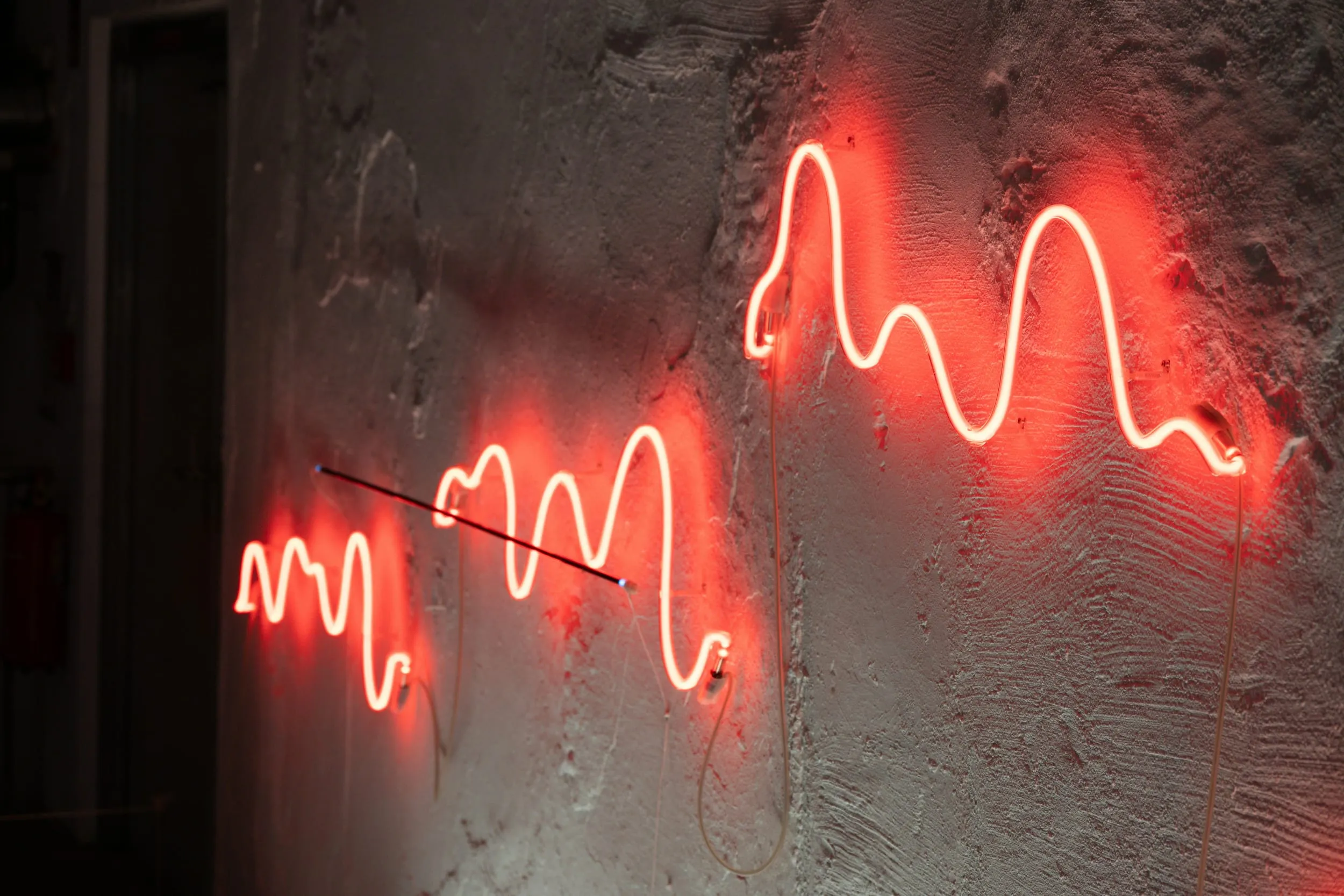 Three red neon waveforms mounted on a concrete wall